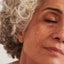 Woman with mature skin applying droplets of rose otto facial oil to deeply hydrate and moisturise